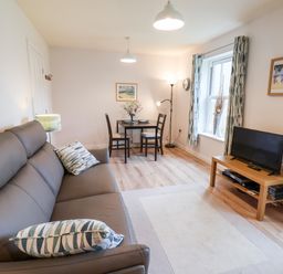 A living room with a grey sofa two chairs a small dining table a TV on a wooden stand and patterned curtains at Kittiwakes The Bay  Filey