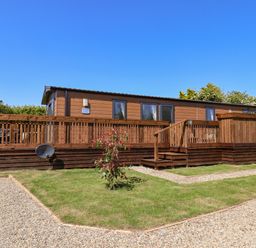 A wooden lodge with a raised deck and steps surrounded by grass and gravel paths at Marigold Lodge in Runswick Bay near Staithes