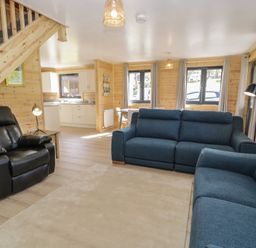 A living room with blue sofas black recliner wooden staircase and kitchen area at Sunset Lodge 5 in Llanbedr