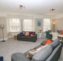A living room with grey sofas colourful cushions a dining table with assorted chairs and paintings on the wall at Chine Heights in Bournemouth