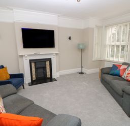 A living room with a wall mounted television above a fireplace two sofas and a blue armchair with cushions at Chine Heights in Bournemouth