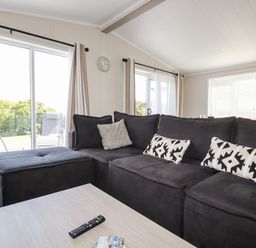 A living room with a large dark sectional sofa and cushions beside sliding glass doors at 63 The Maples in Hewas Water near Sticker