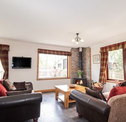 A living room with two sofas a wood burning stove a coffee table and three windows at Lovat Highland Bothy in Beauly