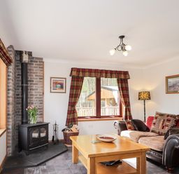 A living room with a wood burning stove next to a window with plaid curtains and a sofa with cushions at Lovat Highland Bothy in Beauly
