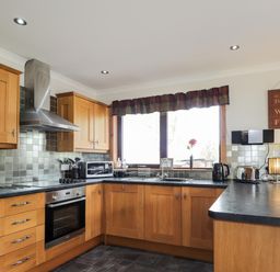 A kitchen with wooden cabinets, black countertops, a window above the sink, and various appliances at Lovat Highland Bothy in Beauly