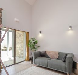 A living room with a gray sofa cushions and a throw blanket near sliding glass doors and a potted plant at Ben Luna Lodge in Drumnadrochit Loch Ness