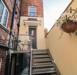 An outdoor staircase leading to a gray door with a small balcony and a hanging basket of flowers at Tower Apartment in Whitby