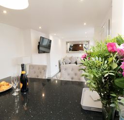 A kitchen counter with a bottle of wine glasses and croissants with a living room and a sofa visible beyond at Tower Apartment in Whitby