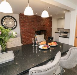 A kitchen with a black countertop island and gray chairs with a brick wall and a clock at Tower Apartment in Whitby