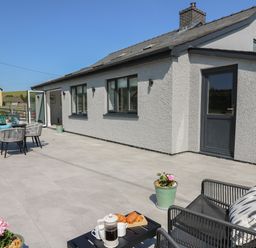 An outdoor patio with a dining table and chairs set near a house with grey walls and windows at Rhiwmynach in Pontarfynach near Aberystwyth