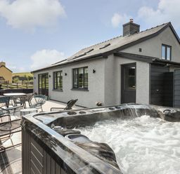 An outdoor patio with a hot tub seating and tables beside a grey house with black windows at Rhiwmynach in Pontarfynach near Aberystwyth