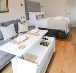 A bedroom with a bed and a sofa with a table set for dining in a room with wooden flooring at The Folly in Linton near Thresfield
