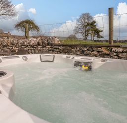 An outdoor hot tub with water bubbling near a stone wall and wire fence with trees beyond at The Folly in Linton near Thresfield