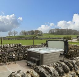 An outdoor patio area with a hot tub surrounded by stone walls and a view of green fields and trees at The Folly in Linton near Thresfield