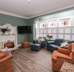 A living room with armchairs sofas a fireplace a television and stained glass windows at South Bay Beach House Bridlington