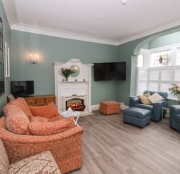 A sitting room with patterned sofas a white electric fireplace a wall mounted TV and windows with stained glass at South Bay Beach House in Bridlington