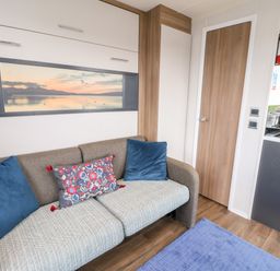 A living room with a sofa and cushions next to a wooden door and kitchen area at Balvicar Beag Balvicar Isle Of Seil