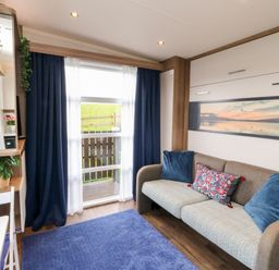 A living room with a sofa cushions a blue rug a window with curtains and a desk with a plant at Balvicar Beag in Balvicar Isle Of Seil