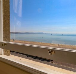 A view from a window overlooking the beach and sea at 123 On The Sea – Victoria’s Place in Weymouth