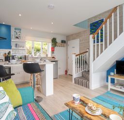 An open plan kitchen and living area with bar stools at a counter a staircase and a television at Blue Waters in Weymouth