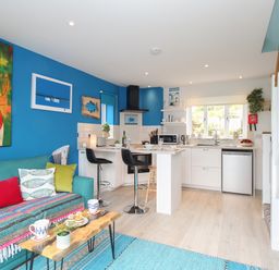 An open plan living room and kitchen with a teal sofa and colorful cushions at Blue Waters in Weymouth