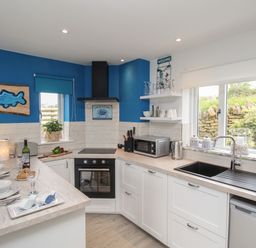 A kitchen with white cabinets blue walls a black oven and countertop appliances at Blue Waters in Weymouth