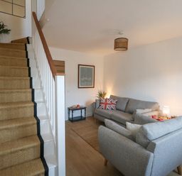 A living room with grey sofas and a staircase with a carpet runner at The Nightingale in Weymouth