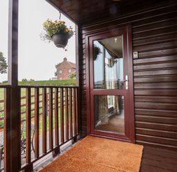 A wooden balcony with a glass door a hanging flower pot and outdoor table and chairs at Handale Banks Farm Lodge in Liverton