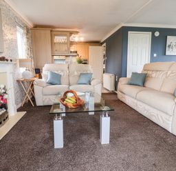 A living room with two beige sofas a glass coffee table with a fruit bowl and a fireplace at Handale Banks Farm Lodge in Liverton