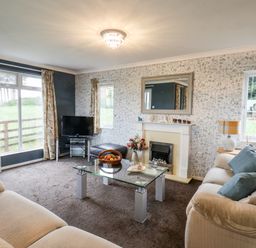 A living room with two beige sofas a glass coffee table a fireplace and a television at Handale Banks Farm Lodge in Liverton