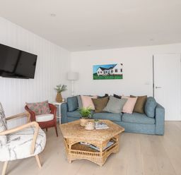 A living room with a blue sofa multiple cushions a wall-mounted TV and a wicker coffee table at 31 Sisial Y Mor in Rhosneigr