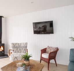 A living room with a wood burning stove two different chairs a wicker coffee table with plants and a wall mounted television at 31 Sisial Y Mor in Rhosneigr