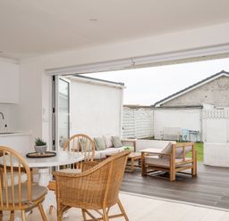 A dining area with chairs and a table next to an open patio with outdoor seating at 31 Sisial Y Mor in Rhosneigr