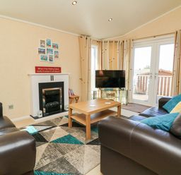 A living room with leather sofas a wooden coffee table a TV on a glass stand a fireplace and patio doors at Mojo Mullacott near Ilfracombe
