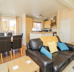 A living room with a black leather sofa and blue and yellow cushions near a wooden dining table with six chairs at Mojo Mullacott near Ilfracombe