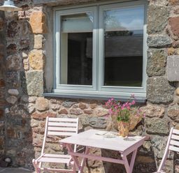 A pink table and two chairs outside a stone cottage with a window and flowers on the table at Traeth Ora in Moelfre