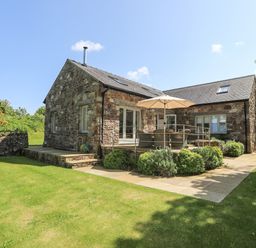 A stone house with a patio umbrella and outdoor seating in a garden at Traeth Ora in Moelfre