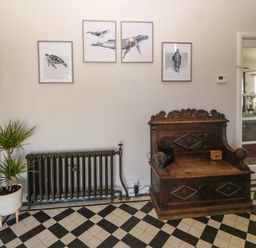 A room with a vintage wooden bench a radiator potted plant framed marine animal prints and a tiled floor at Wig Carna in Holyhead