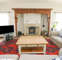 A living room with a wooden coffee table a red patterned rug beige sofas a fireplace and a television at Wig Carna in Holyhead