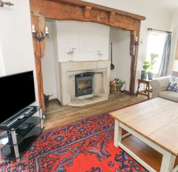 A living room with a fireplace a wooden coffee table a television on a stand and a sofa with cushions at Wig Carna in Holyhead
