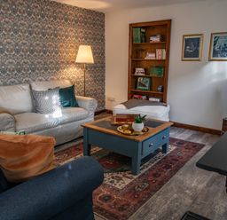 A living room with sofas a blue table a floor lamp and a bookshelf at Fern Cottage in Muddiford near West Down