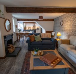 A living room with sofas a coffee table and a fireplace opening into a dining area and kitchen at Fern Cottage in Muddiford near West Down