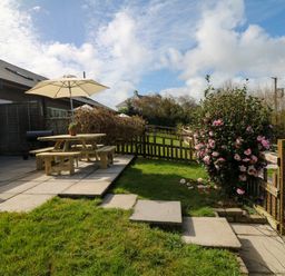 A garden with a wooden picnic table and umbrella on a patio near a flower bush and a wooden fence at Fern Cottage in Muddiford near West Down
