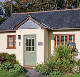 A small cottage with a green door flanked by two windows and surrounded by plants at Inny Brook Cottage in Davidstow near Camelford
