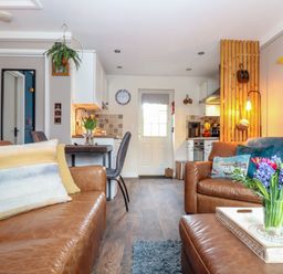 A living room with brown leather sofas a vase of flowers on a tray and a kitchen area at Inny Brook Cottage Davidstow near Camelford
