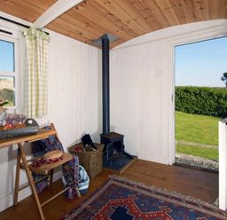 An interior room with wooden ceiling and floor a small stove and a doorway open to a grassy yard at Shepherd's Hut in Southerndown near St Brides Major