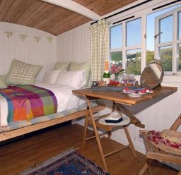 A small bedroom with a single bed a wooden floor a folding table and a chair at Shepherd's Hut in Southerndown near St Brides Major