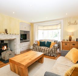 A living room with a wooden table a sofa with yellow pillows a loveseat with blue and yellow pillows a fireplace and a wooden sideboard at The Farmhouse in Felmingham near North Walsham