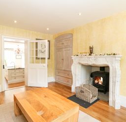 A living room with a wooden coffee table a fireplace with a wood stove an open door leading to a kitchen at The Farmhouse in Felmingham near North Walsham