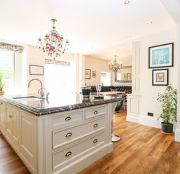 A kitchen island with a sink and drawers in a dining area with chandeliers and framed pictures at The Farmhouse in Felmingham near North Walsham